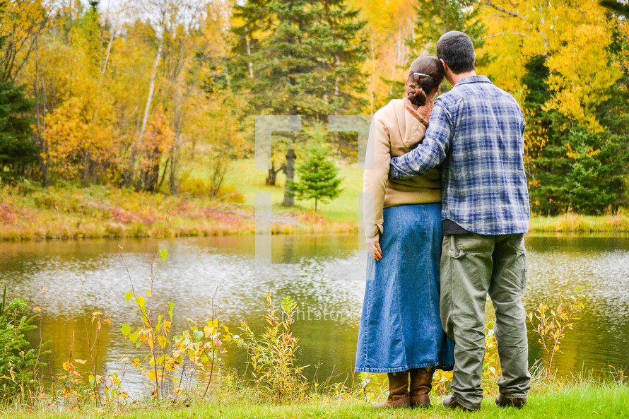 a couple standing together near a lake in fall 