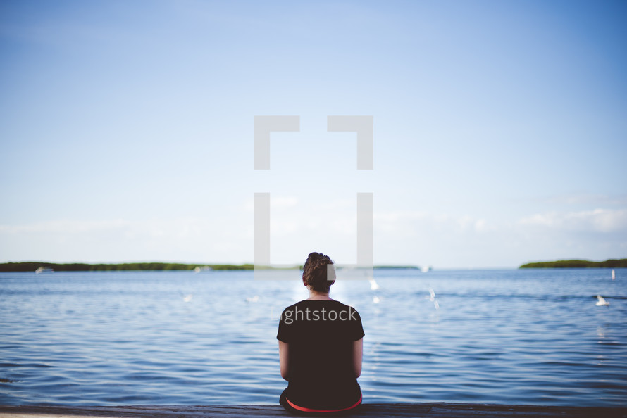 a woman sitting on a dock looking out at the water 
