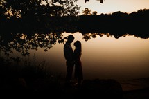 silhouette of a couple standing in front of a lake at dusk 