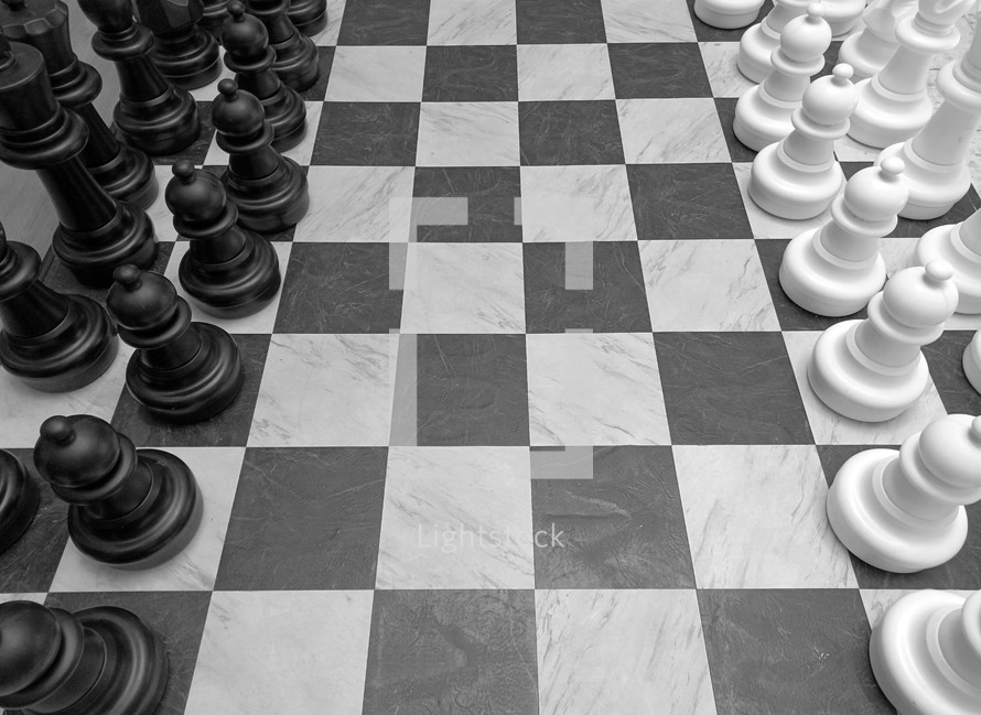 A black and white image of a huge chess board with chess pieces in black and white on a checkered black and white chess board that takes up about 10 feet of floor space symbolizing the game of life, life and death, good and evil, risk and chance and strategy and planning. All the things that make up life and thinking through moves that we make that can affect our spiritual and physical as well as mental well being. 

I saw this huge chess board at a local shopping mall and it just captured my imagination and had to photograph it. It reminded me of the game of life and the choices we have to make to affect our future as well as the spiritual battle between good and evil that we deal with in this life and the next. 
