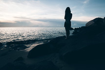 a girl standing on a beach at dusk 