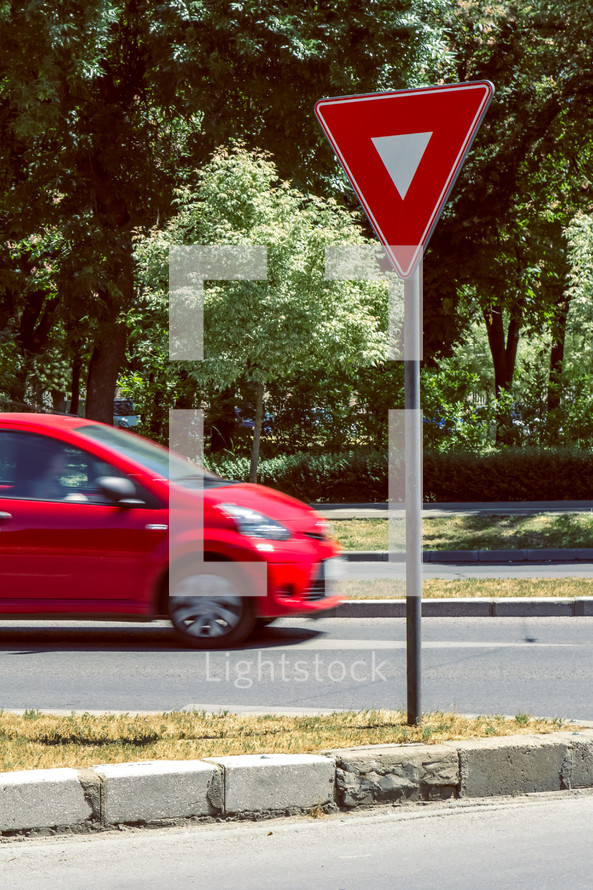 Yield sign near a crossroad with a red rushing car. Chromatic contrasts
