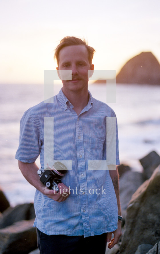 a man holding a camera by a shore 