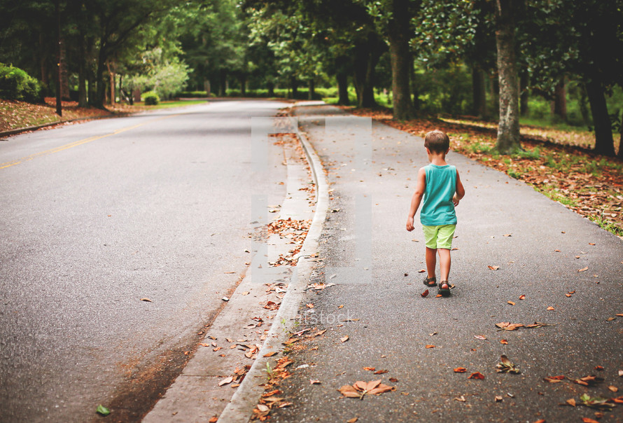 a little boy walking down a neighborhood sidewalk 