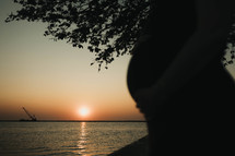 a pregnant silhouette against a sun setting on the lake 