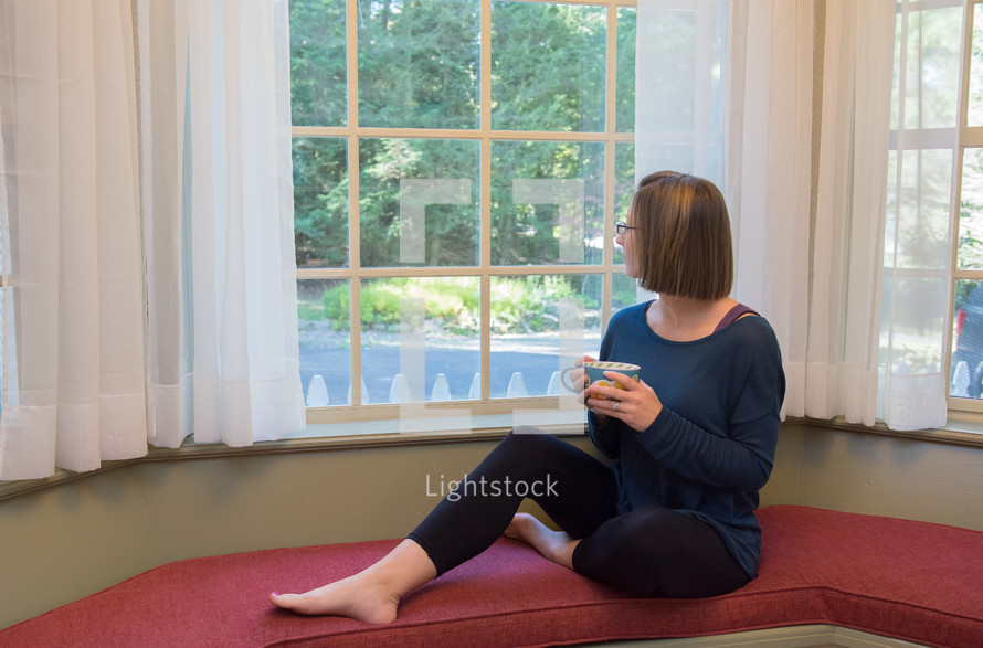 a woman sitting in a window seat looking out a window thinking 