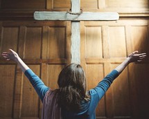 a woman with hands raised standing in front of a cross 