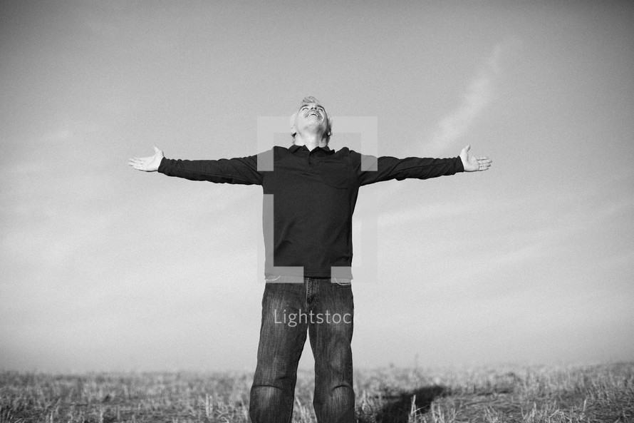 elderly man standing outdoors in a field with his hands outstretched in worship to God