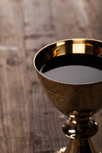 A golden communion goblet full of wine on a wooden surface.