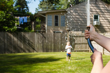 a mother spraying a toddler boy with a hose 