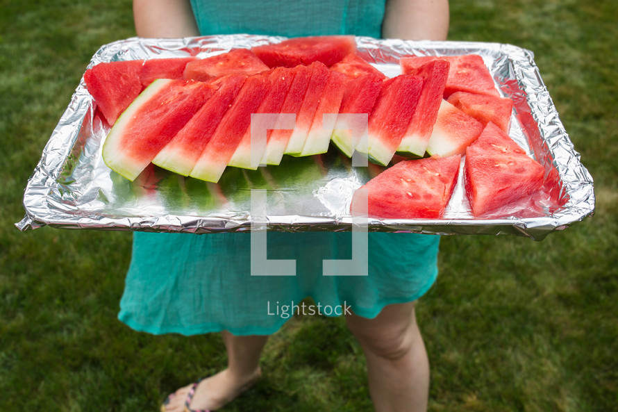 a woman holding a tray of cut watermelon 