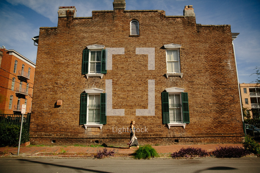 woman walking on a sidewalk in front of a brick building 