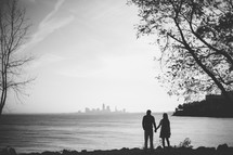a couple holding hands with view of a city skyline across the water 