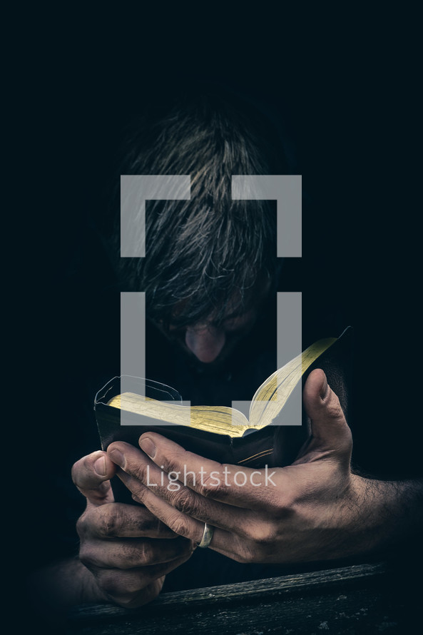 Man praying with head bowed before an open Bible held in both hands.