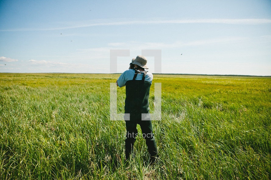 man taking a picture with a camera in a coastal field of grass 