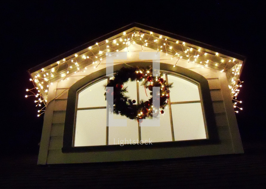 A Christmas Wreath hangs in a window decorated with Christmas lights to light up the night sky and bring a feeling of warmth to the cool winter air as people get ready for the Christmas holidays. 