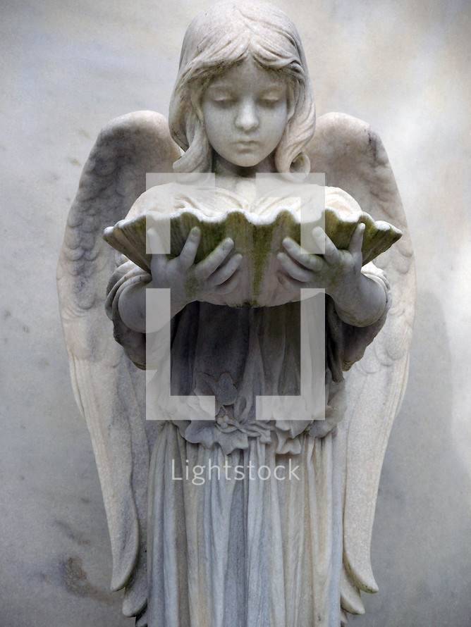 An Angelic female character statue holding an oyster shell in a historic cemetery in the southeastern United States as a grave marker and symbol of eternal rest among the Heavenly host of angels and God. 