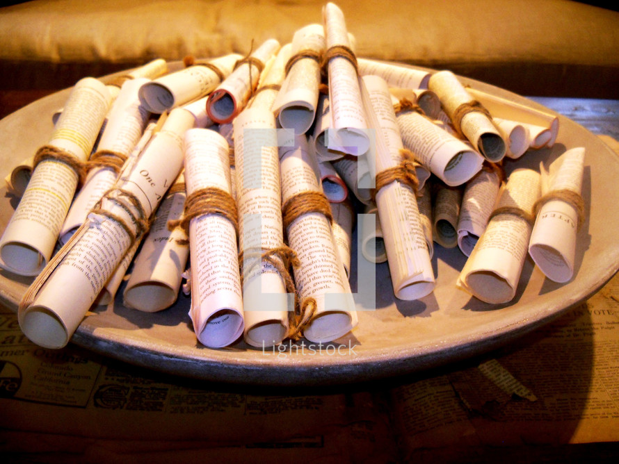 A bowl filled with old rolled up paper manuscript scrolls with the word of God and bible lessons printed to give out to people. In the early days, the word of God was written on parchments of scrolls of linen paper such as papyrus dating as far back as the early church. These scrolls are a reminder of how the word has endured the test of time and that the word of God is timeless enduring forever and a reminder that God's word will not return unto Him void but accomplish that which He pleases. Which is why we need to share the word of God as often as we can to tell people about Jesus.  