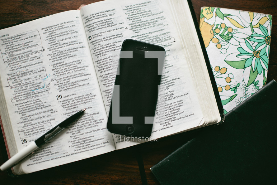 open Bible, pen, journal, and cellphone