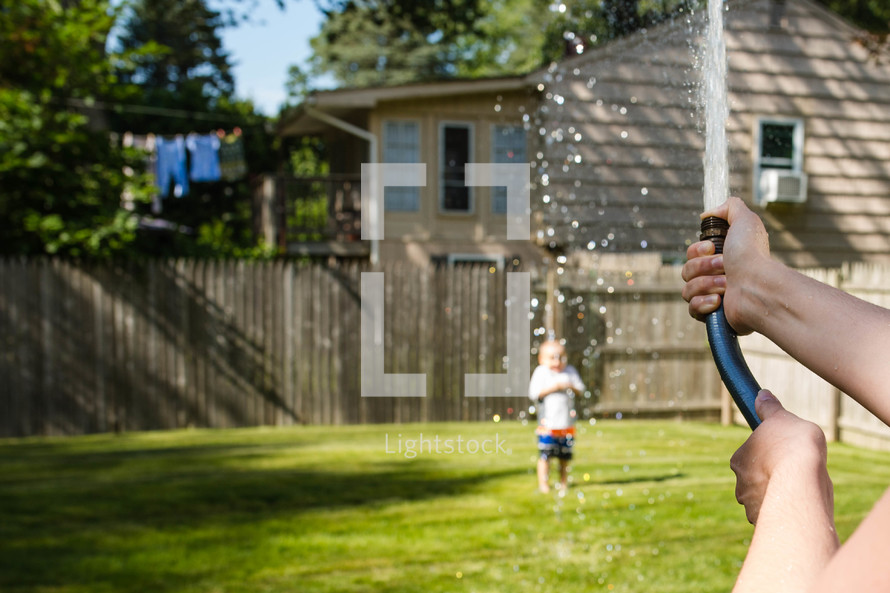 a mother spraying a toddler boy with a hose 