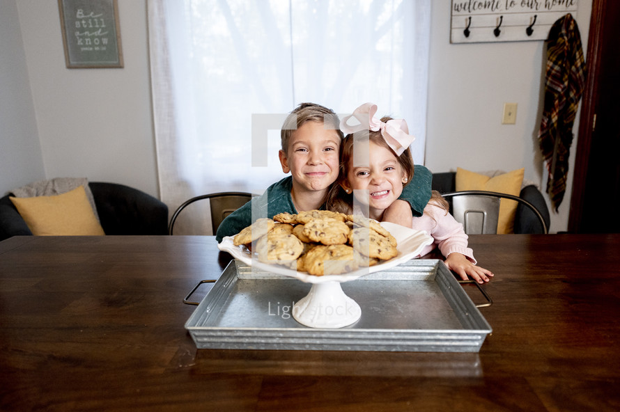 a brother and sister near a plate of cookies 