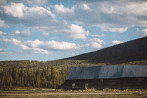A large old log barn amid tree covered hills.
