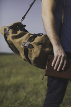 a man walking carrying a Bible and a bag though a field 