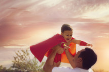a father holding up his son in a cape 
