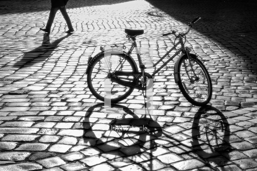 Shadow of a bicycle on cobblestone pavement at morning. Black and white image
