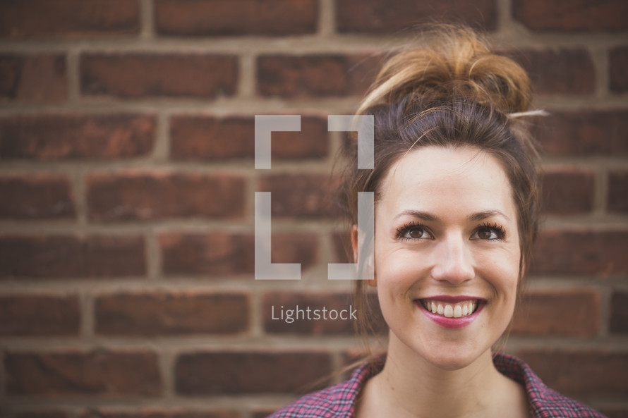A smiling woman standing in front of a brick wall.