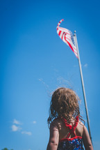 little girl looking up at an American flag on a flagpole 