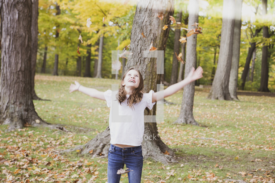 girl throwing fall leaves up outdoors 