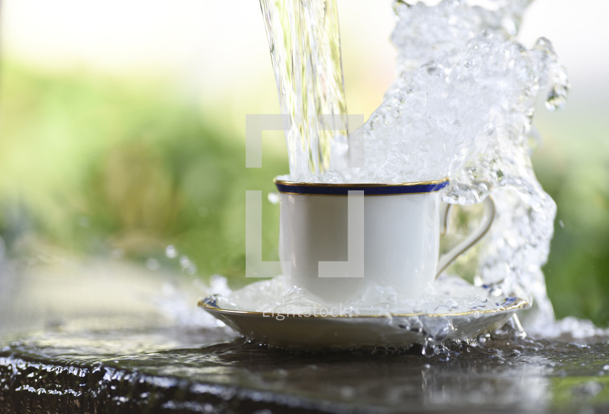Water being poured and overflowing from a cup and saucer.