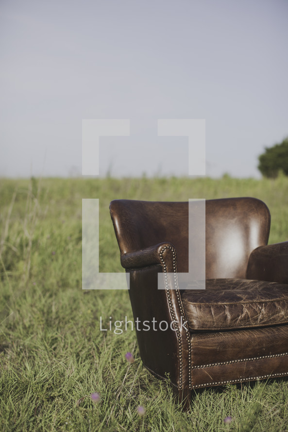 a leather chair alone in a field of tall grass 