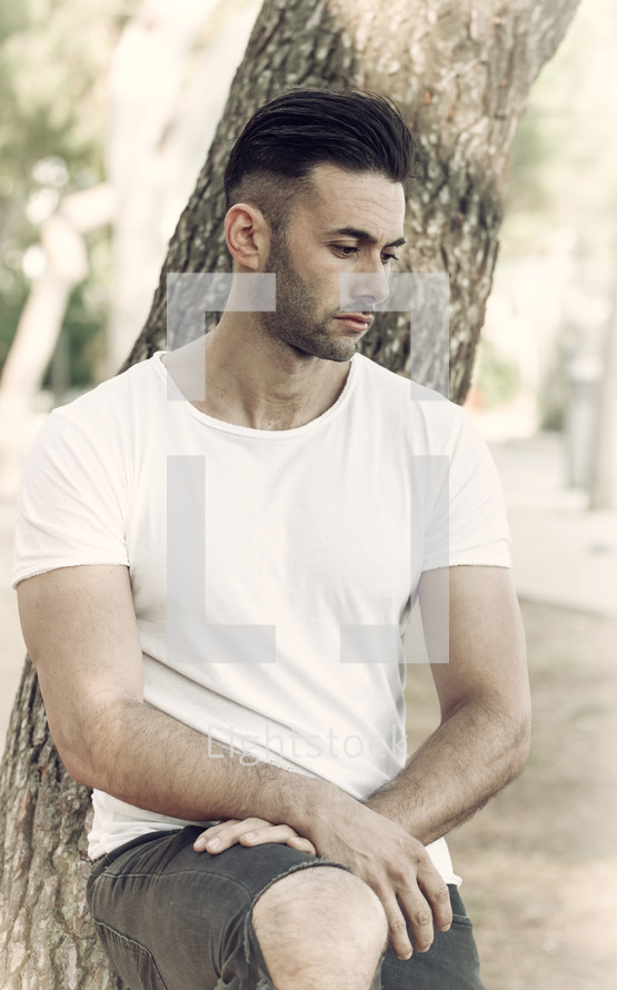 Sad and thoughtful man leaning against the trunk of a tree.