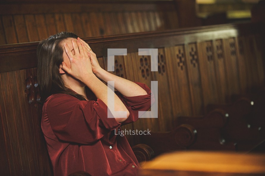 a woman covering her face sitting alone in a church 