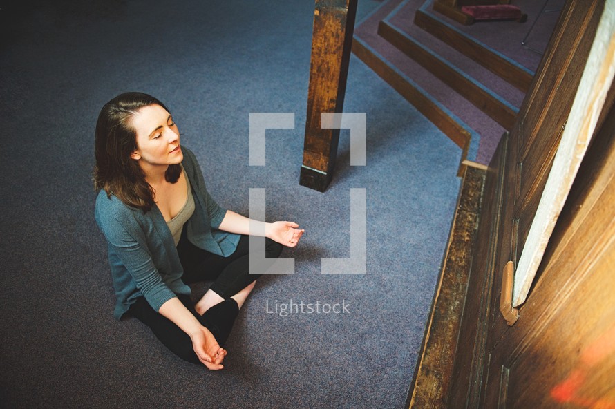 a woman sitting on the floor in prayer in a church 