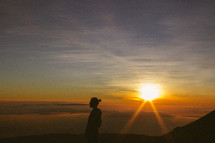 side profile silhouette of a man standing on a mountaintop at sunrise 