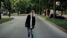 a young woman in torn jeans walking down a neighborhood street 
