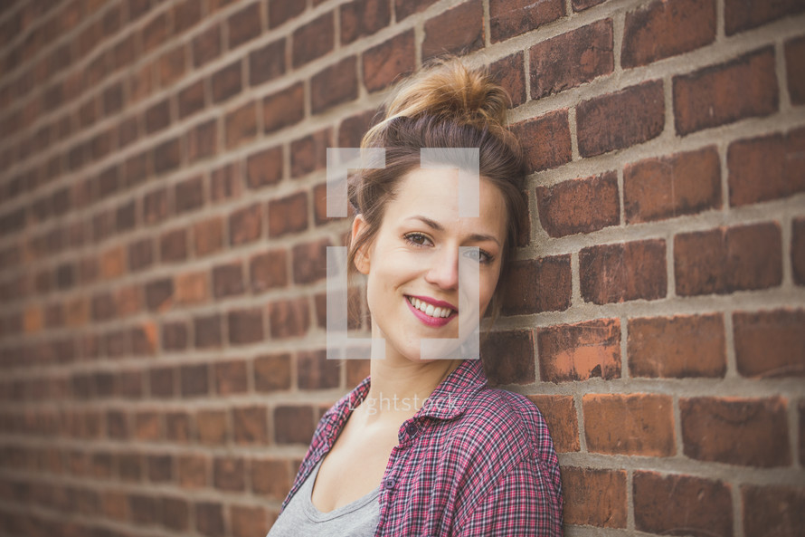 A smiling young woman standing against a brick wall.