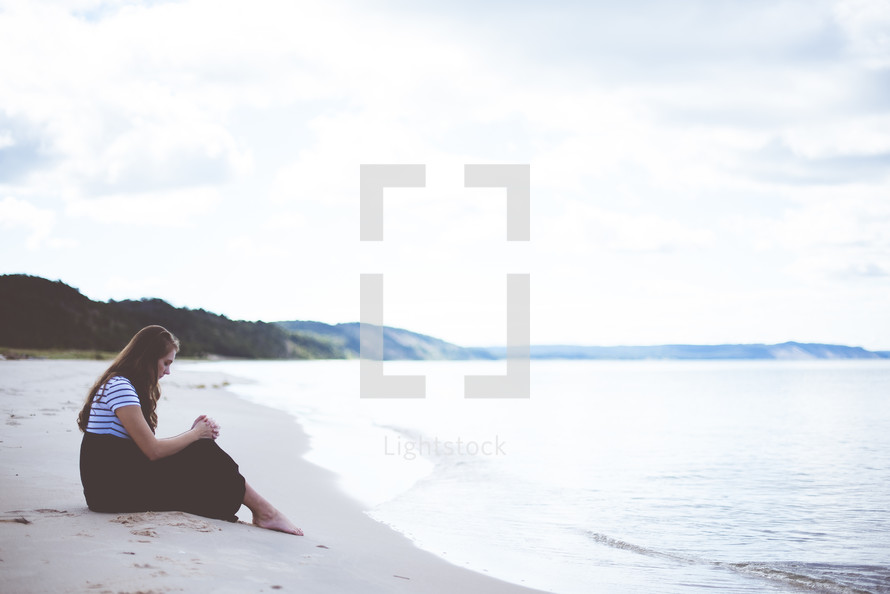 woman sitting on a beach praying 