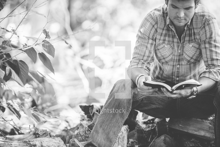 man reading a Bible next to pile of firewood 