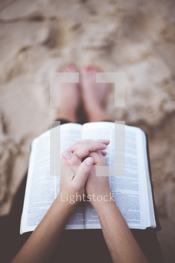 man praying over a Bible on a beach 