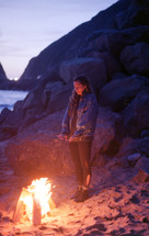 a woman standing by a fire on the beach 