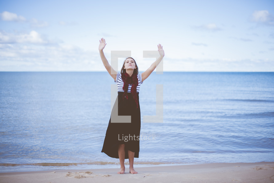 a woman with hands raised standing on a beach 