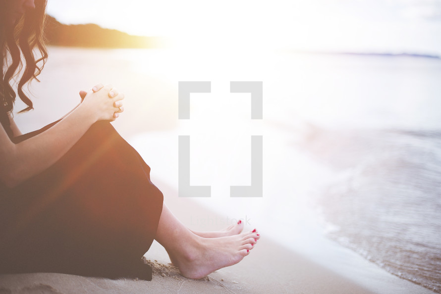 a woman sitting on a beach praying 