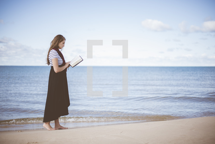 a woman standing on a beach reading a Bible 