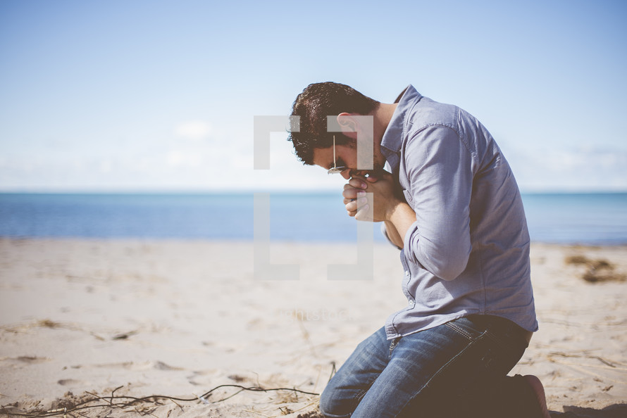 man kneeling on a beach praying 