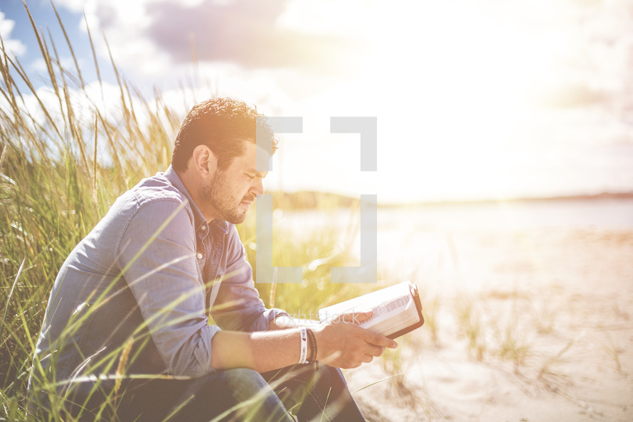 a man sitting on a beach reading a Bible 
