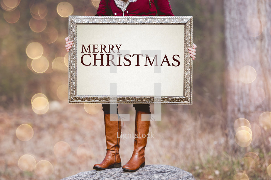 a woman holding a sign the reads Merry Christmas 